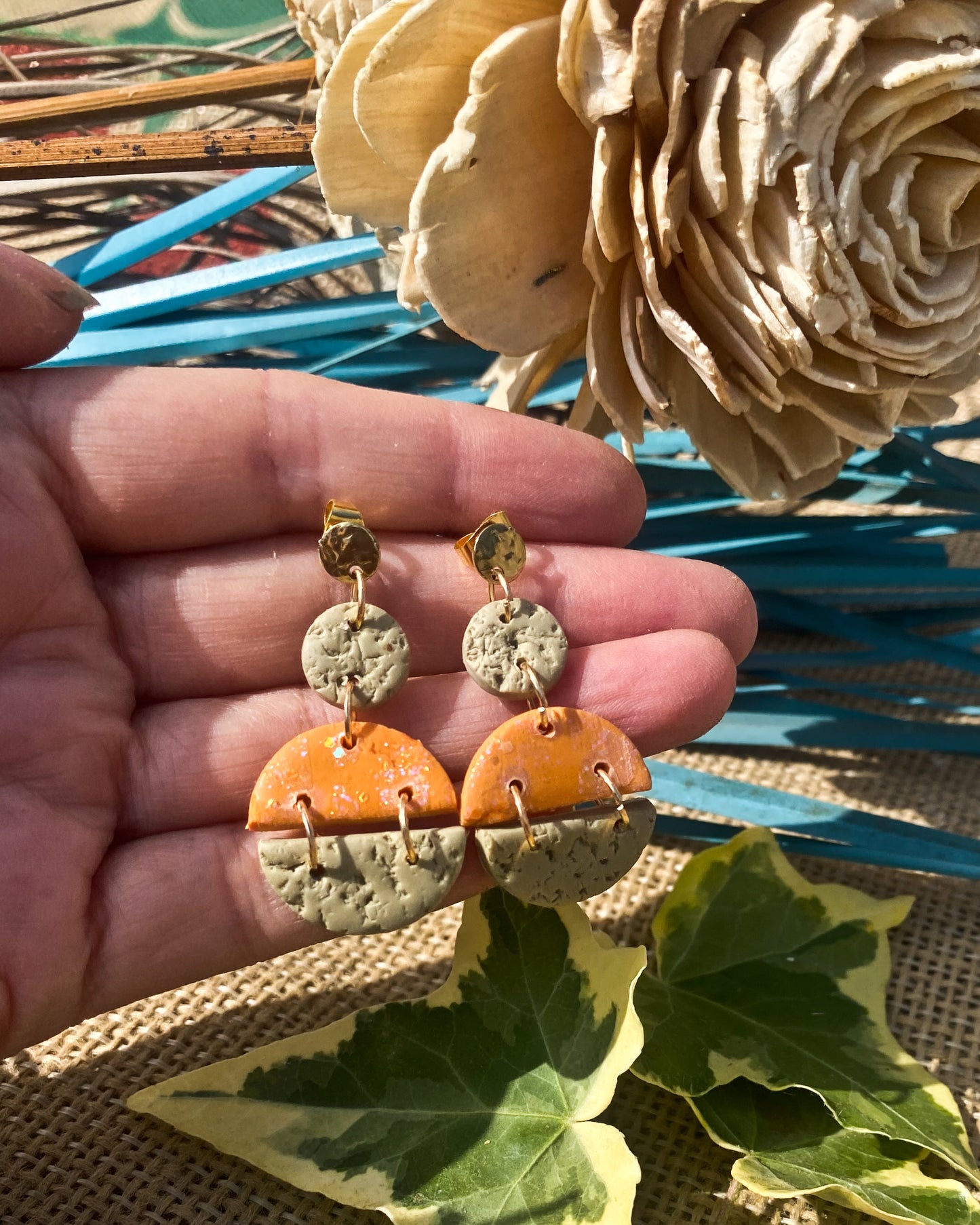Handmade orange and sage textured polymer clay drop earrings with gold studs held in hand