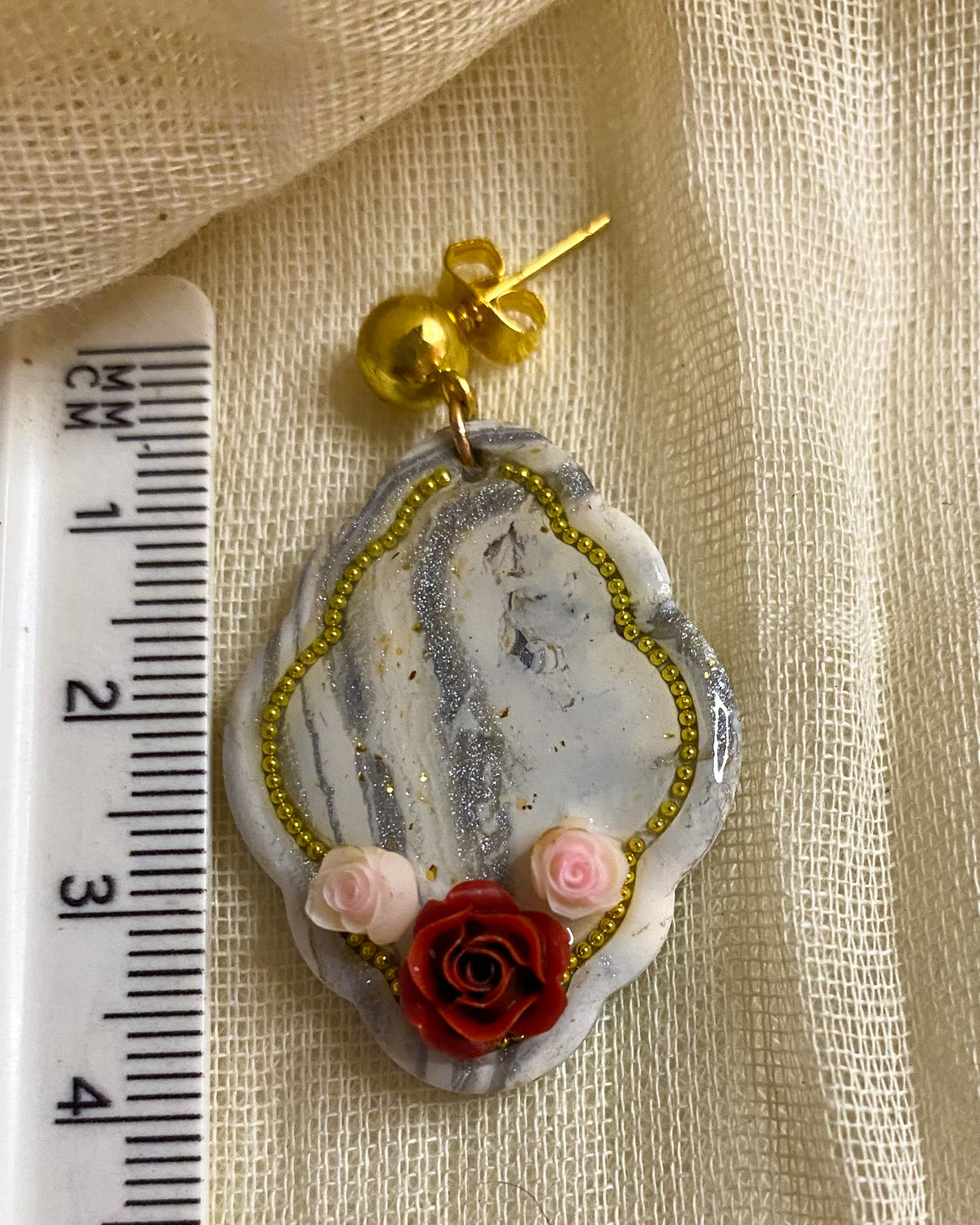 Close-up of white and silver marbled clay earring with red rose, pink flowers and gold-tone beaded outline