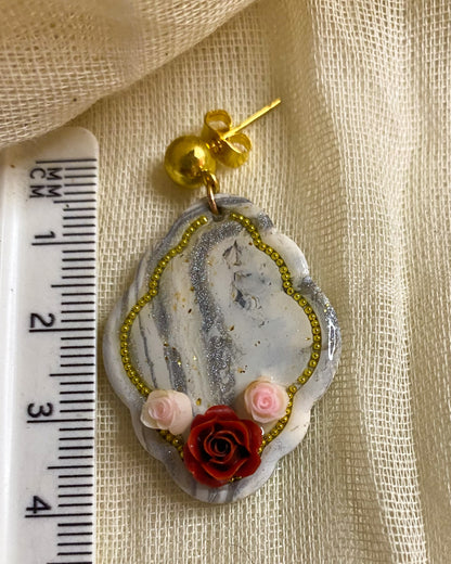 Close-up of white and silver marbled clay earring with red rose, pink flowers and gold-tone beaded outline